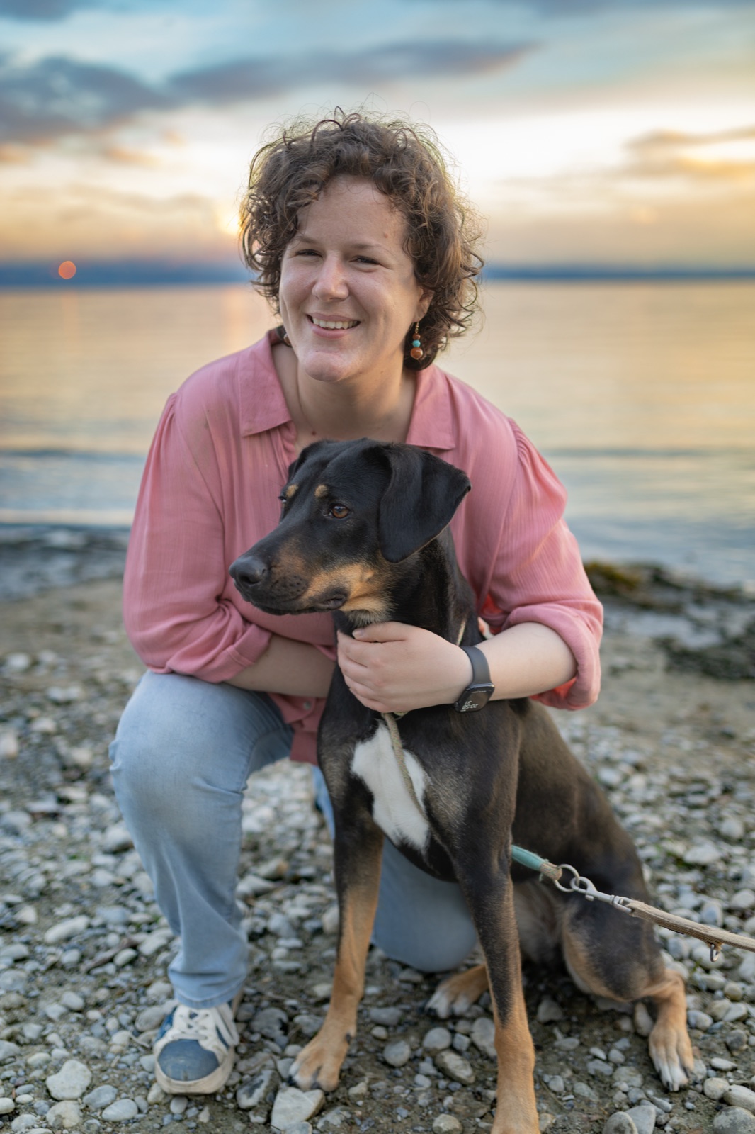 Frau mit ihrem Hund am Kiesufer des Bodensees in der Abenddämmerung